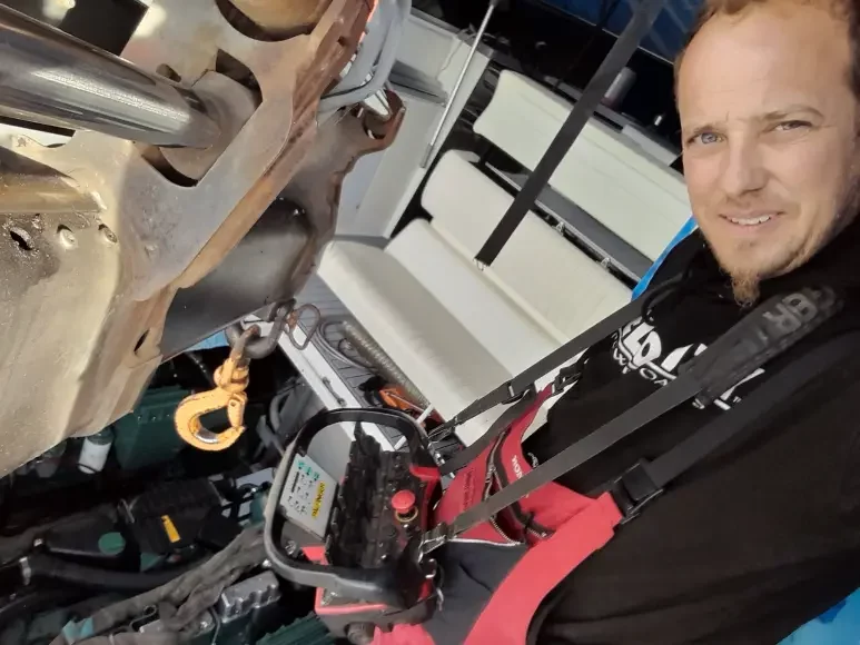 Homme souriant en combinaison rouge effectuant maintenance de bateau.