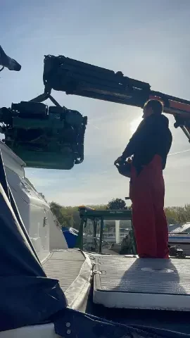 Technicien manœuvrant une grue pour déplacer un moteur sur un bateau.