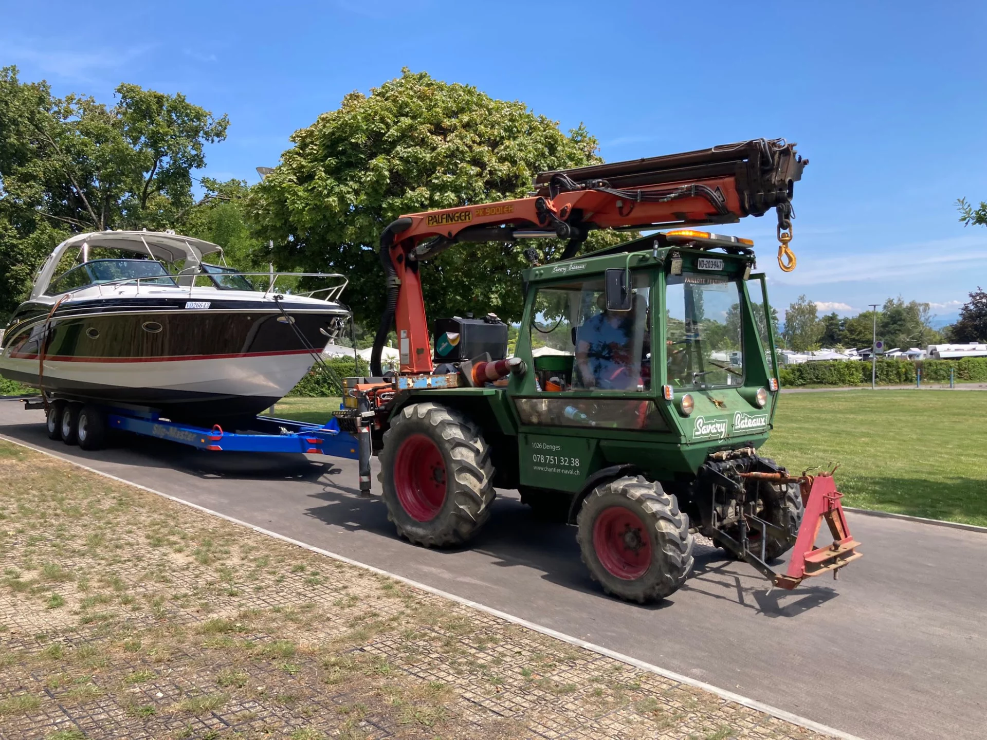 Tracteur vert transportant un bateau à moteur sur une remorque.