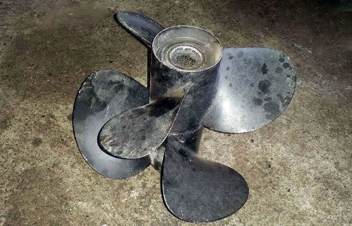 Hélice de bateau en métal sur un sol en béton.
