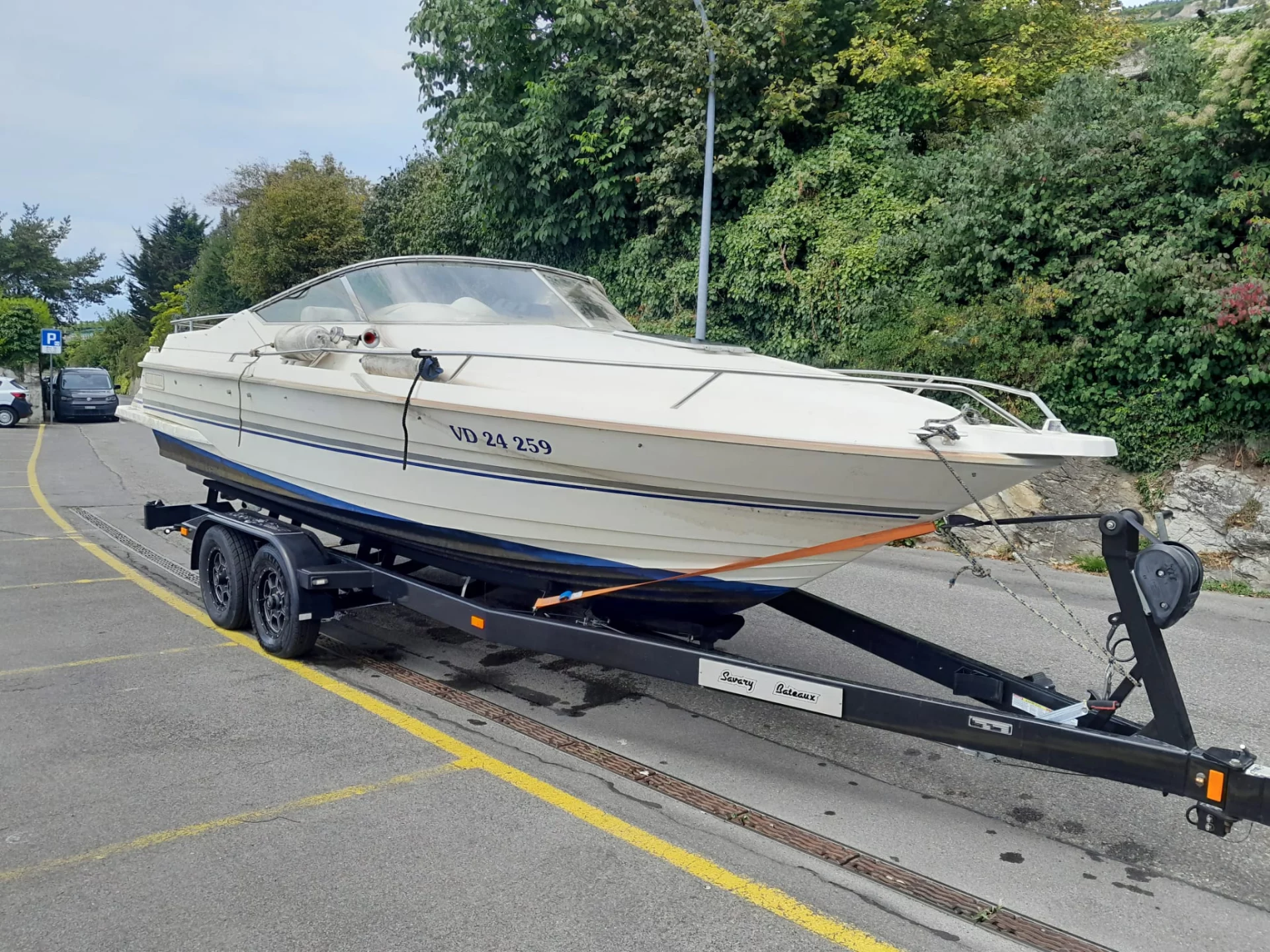 Bateau blanc sur une remorque stationnée près d'une route bordée de verdure.