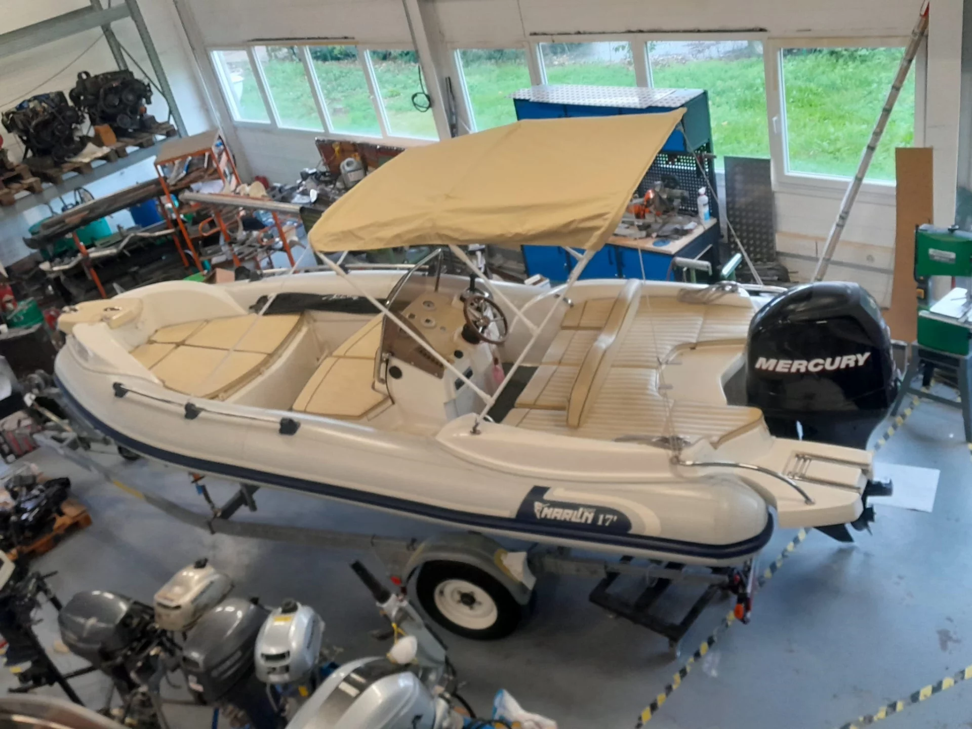 Bateau pneumatique blanc avec moteur Mercury dans un atelier.