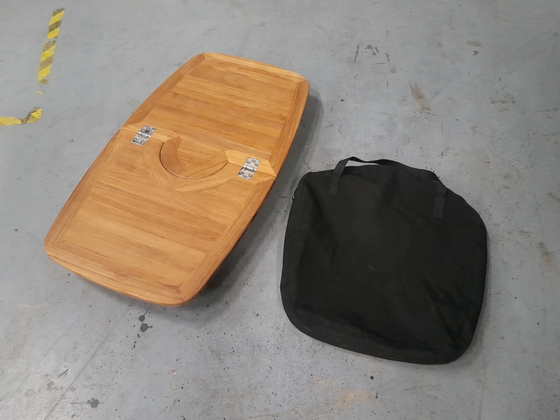 Planche de bois pliée avec sac noir sur sol en béton.