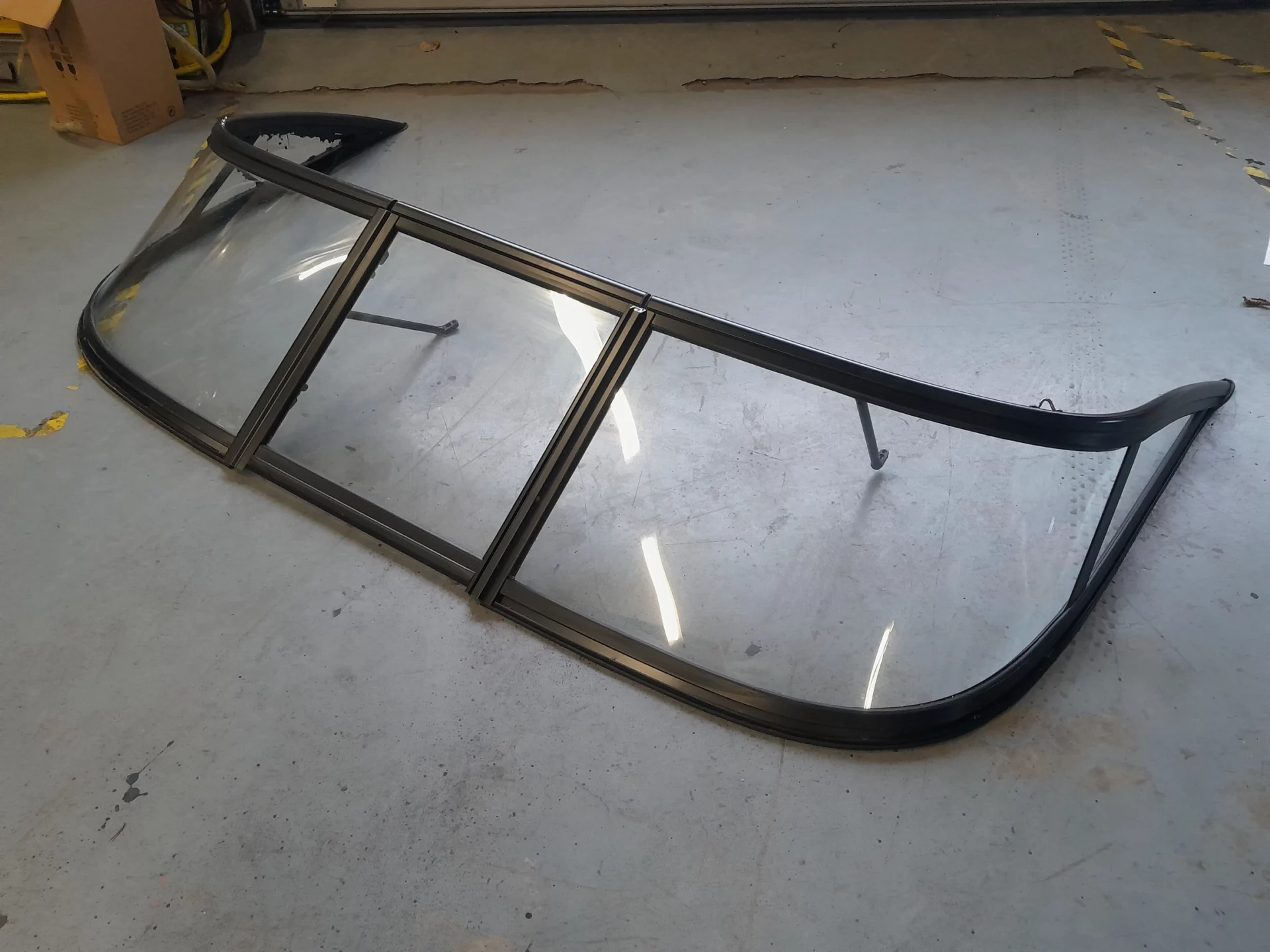 Pare-brise de voiture en verre courbé posé au sol d'un atelier.